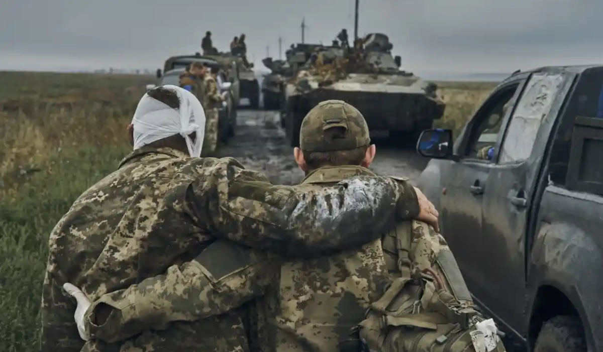 “A Ukrainian soldier helps a wounded comrade as troops move down a road in the Kharkiv region.” Photograph by Kostiantyn Liberov/AP.